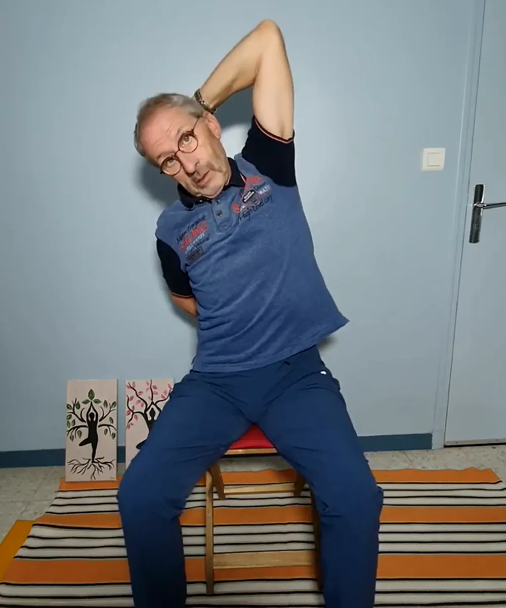 Jean-Louis Sitjar assis sur un tabouret, en étirement latéral, un bras au-dessus de la tête